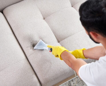 Dry cleaning worker removing dirt from sofa indoors