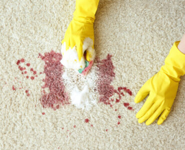 Hands in rubber gloves cleaning carpet with sponge and detergent