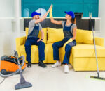 Satisfied couple of cleaners in blue uniforms giving each other high five and continuing to clean the floor in the kitchen.