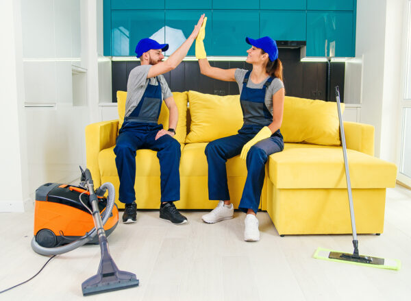 Satisfied couple of cleaners in blue uniforms giving each other high five and continuing to clean the floor in the kitchen.